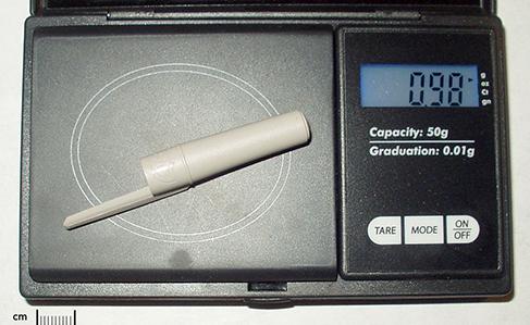 A plastic pen cap is sitting on a digital scale and has a measured mass of 0.98 grams.