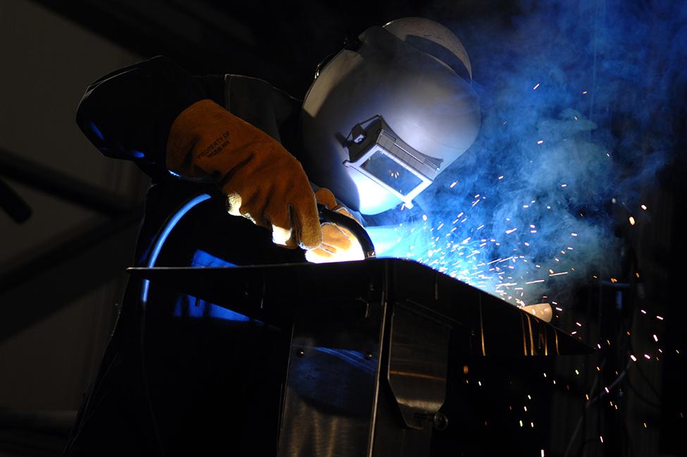Sparks fly as a welder wearing a mask welds.