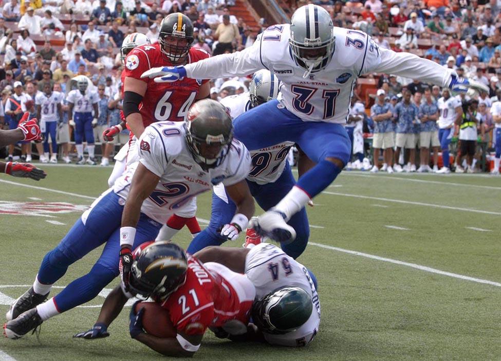 A photograph shows a football game with four football players trying to tackle a fifth player. A crowd is shown in the background.