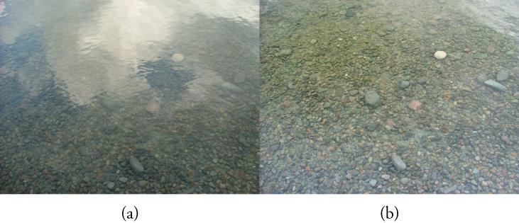This figure shows two photographs arranged side by side. The left photograph, labeled '(a)', shows a river bed that looks hazy because of interfering gray and white patches. The right photograph, labeled '(b)', shows the same area of the river bed with almost no interfering gray patches, so that the pebbles on the bed are clearly visible.