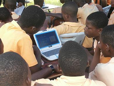 This photograph shows several students gathered around a single laptop that has been powered with solar energy.