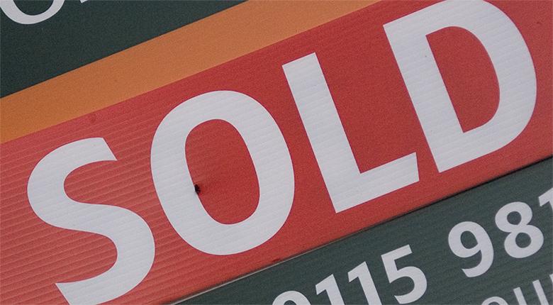 This image is photograph of a woman holding a 'sold' sign.
