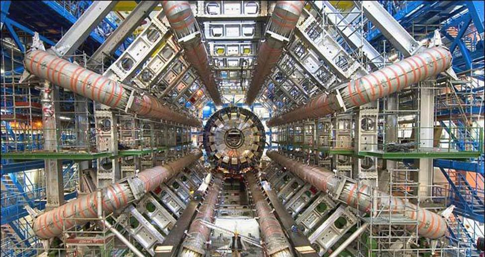 The photograph shows a series of tubes and structural elements that make up the Large Hadron Collider. The five staircases on the sides of the collider show the very large size of the experimental device.