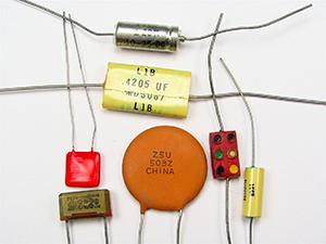 This is a photograph showing seven small capacitors, of varying shapes and colors, usually found in electronic circuits.