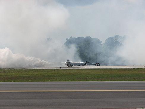 A photograph of a United States Air Force jet car is shown speeding down a track. Smoke is billowing from the back end.