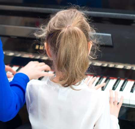 Image of girl playing piano next to an instructor