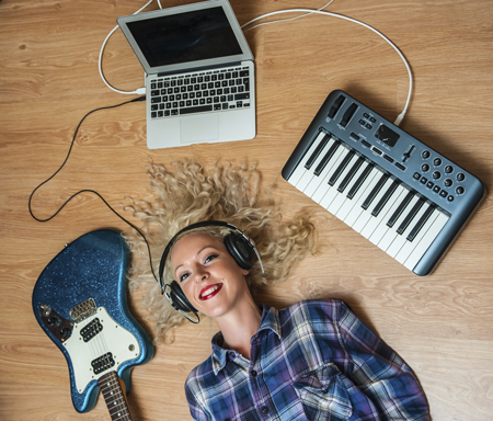 Image of young student with headphones, laptop, guitar, and keyboard