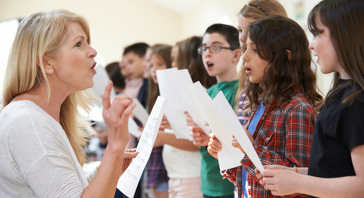 Image of choir teacher with a group of students singing with sheet music