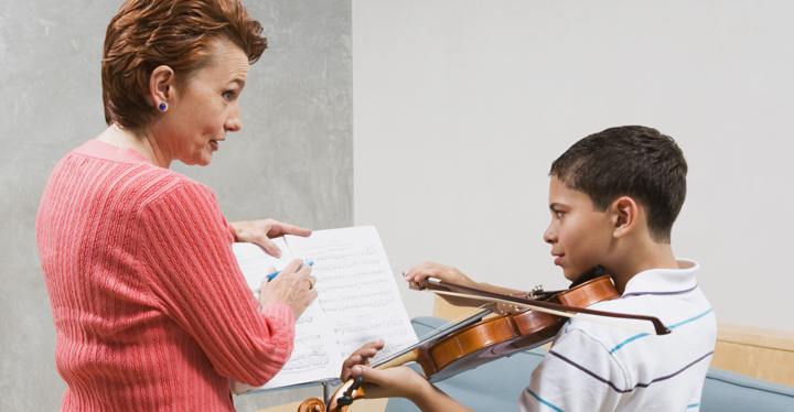 Image of a student playing the violin with guidance from his instructor
